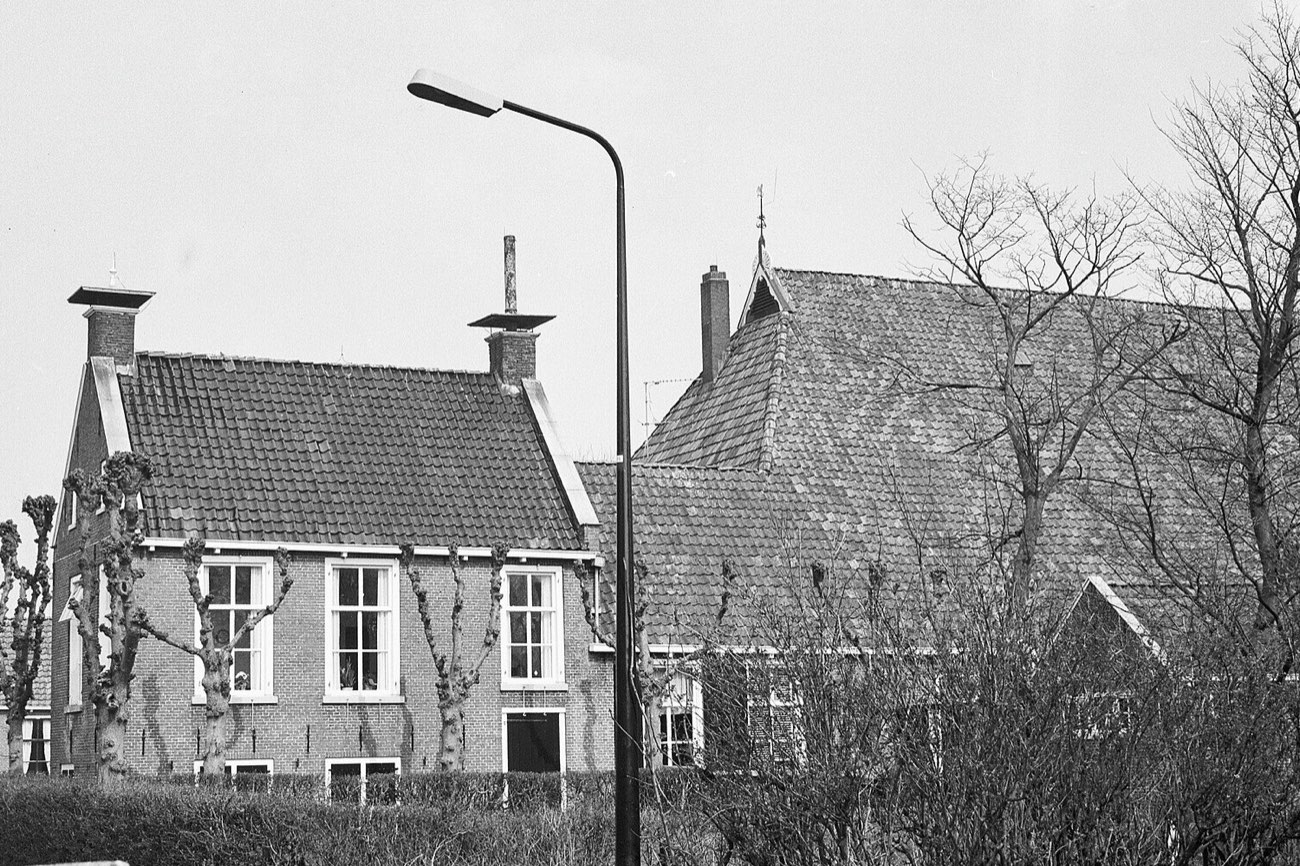 Zwart-witfoto uit 1967 van een Friese boerderij bij Dekema State in Jelsum: bakstenen woonhuis en schuurdak achter een haag, met knotbomen en een straatlantaarn op de voorgrond.