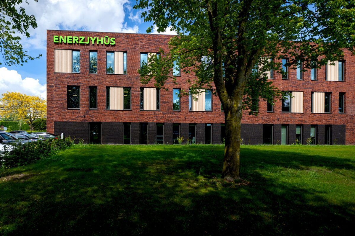 Bakstenen gevel van Enerzjyhûs met houten raamnissen en de naam in het groen; drie bouwlagen onder een blauwe lucht.