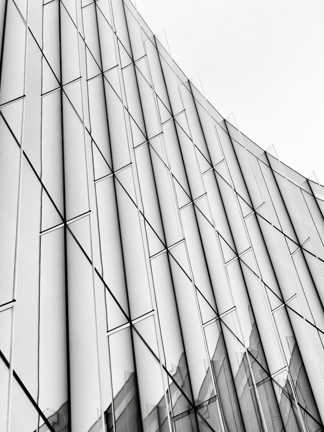 Strak, supermodern gebouw: een licht gebogen glasgevel met een fijn ritme van verticale lijnen tegen een heldere lucht.